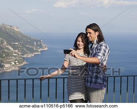 Italy, Ravello, Palazzo Sasso, Portrait of smiling couple photographing themselves with coastline in background View Large Photo Image Stock Photograph - Italy, Ravello, Palazzo Sasso, Portrait of smiling couple photographing themselves with coastline in background. Fotosearch