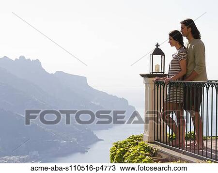Stock Image - Italy, Ravello, Young couple on balcony overlooking coast. Fotosearch