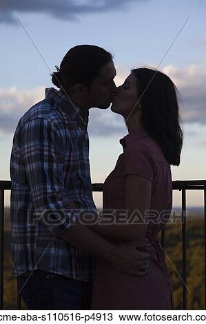 Stock Image - Italy, Tuscany, Couple kissing on terrace at dusk. Fotosearch