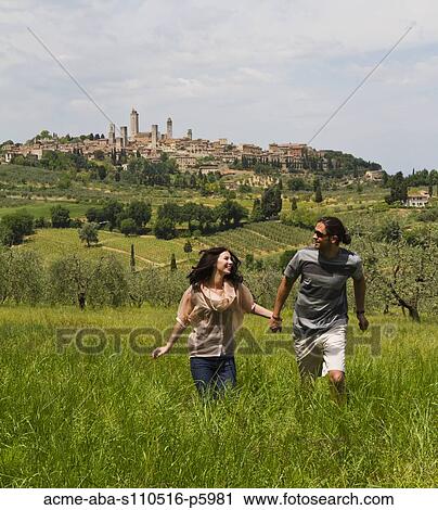 Italy, Tuscany, San Gimignano, Young couple walking on meadow View Large Photo Image Stock Image - Italy, Tuscany, San Gimignano, Young couple walking on meadow. Fotosearch