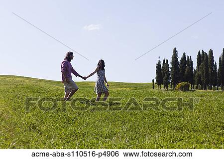 Stock Photograph - Italy, Tuscany, Val D'Orcia, Couple walking in meadow. Fotosearch