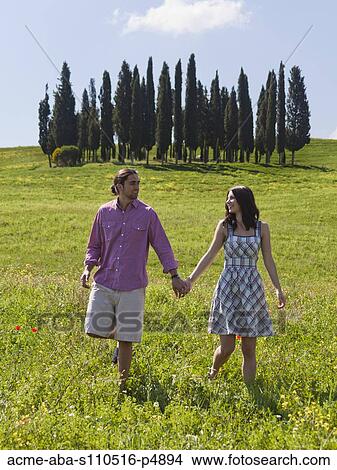 Italy, Tuscany, Val D'Orcia, Young couple walking on meadow View Large Photo Image Picture - Italy, Tuscany, Val D'Orcia, Young couple walking on meadow. Fotosearch