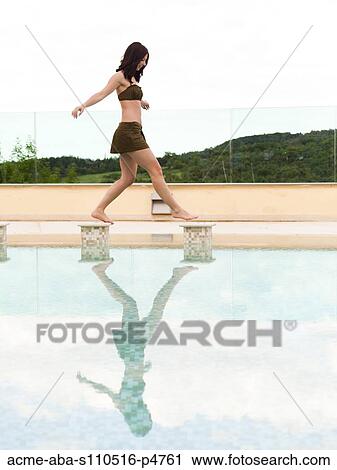 Stock Image - Italy, Tuscany, Woman balancing on edge of swimming pool. Fotosearch