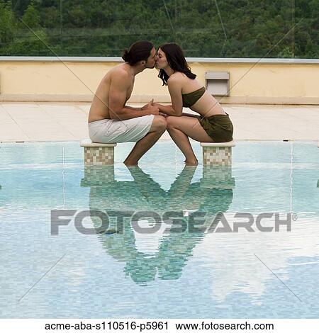 Stock Image - Italy, Tuscany, Young couple kissing in pool. Fotosearch