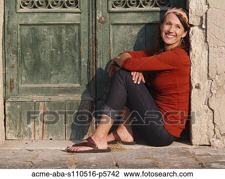 Stock Image - Italy, Venice, Mature woman sitting by old green door. Fotosearch