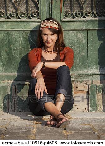 Stock Photograph - Italy, Venice, Portrait of woman sitting by wooden door in old town. Fotosearch