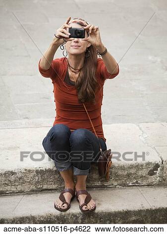 Stock Image - Italy, Venice, Woman using digital camera on steps. Fotosearch