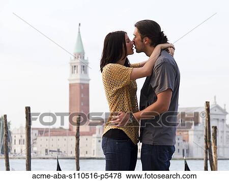 Stock Photo - Italy, Venice, Young couple kissing in front of San Giorgio Maggiore Church. Fotosearch