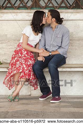 Stock Image - Italy, Venice, Young couple kissing on bench. Fotosearch