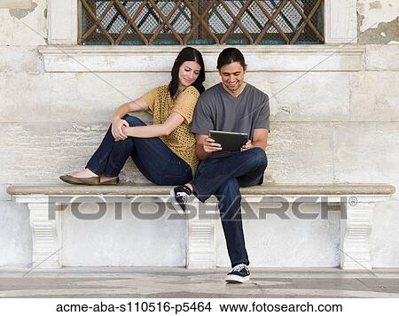 Italy, Venice, Young couple sitting on bench, using digital tablet View Large Photo Image Picture - Italy, Venice, Young couple sitting on bench, using digital tablet. Fotosearch