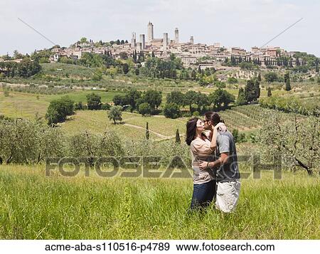 Italy, Young couple kissing in field with old town in background View Large Photo Image Stock Photo - Italy, Young couple kissing in field with old town in background. Fotosearch