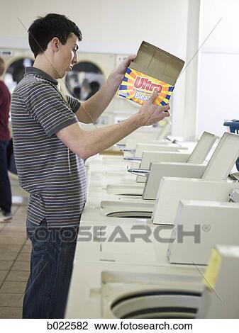 Stock Image - man doing laundry at a laundromat. Fotosearch