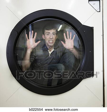 Picture - man inside a commercial clothes dryer at a laundromat. Fotosearch