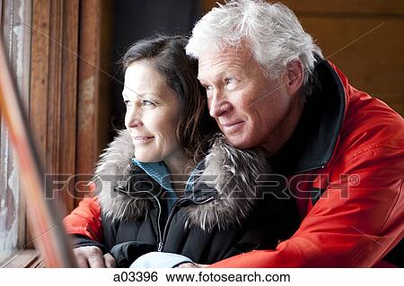 Mature couple looking out of window and embracing View Large Photo Image Stock Photograph - Mature couple looking out of window and embracing. Fotosearch