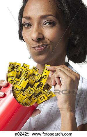 Stock Photography - Mid adult woman holding container with mini tape measures instead of french fries. Fotosearch