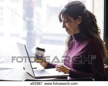 One mid adult woman drinking coffee next to laptop in cafe View Large Photo Image Stock Photo - One mid adult woman drinking coffee next to laptop in cafe. Fotosearch