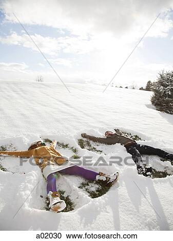 Stock Image - Orem, Utah, USA, young couple making snow angels. Fotosearch