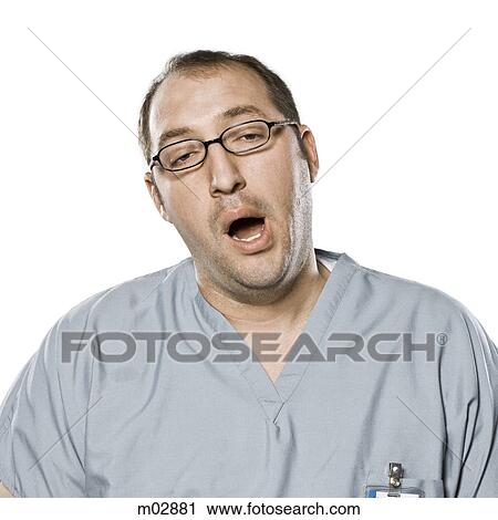 Stock Image - Portrait of yawning man in surgical scrubs, studio shot. Fotosearch