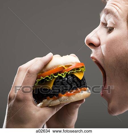 Side view of young man about to bite a tire hamburger, close up View Large Photo Image Picture - Side view of young man about to bite a tire hamburger, close up. Fotosearch