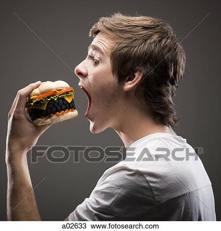 Side view of young man about to bite a tire hamburger View Large Photo Image Stock Image - Side view of young man about to bite a tire hamburger. Fotosearch