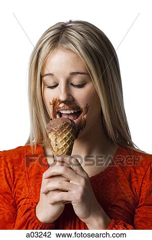 Stock Image - Studio portrait of young woman eating ice cream. Fotosearch