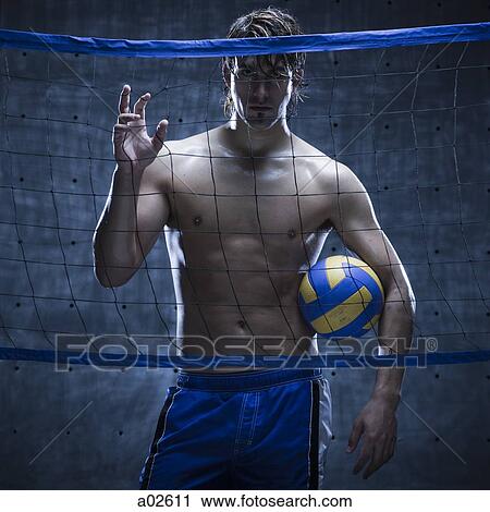 Stock Image - Studio shot of volleyball player standing behind net. Fotosearch