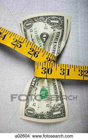 Studio shot of yellow measure tape squeezing two one dollar bills View Large Photo Image Picture - Studio shot of yellow measure tape squeezing two one dollar bills. Fotosearch