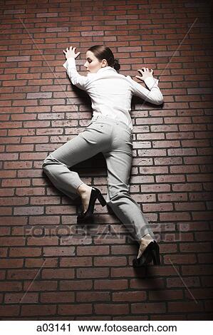 Stock Image - Studio shot of young woman climbing up brick wall. Fotosearch