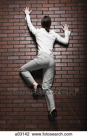 Stock Image - Studio shot of young woman climbing up brick wall. Fotosearch