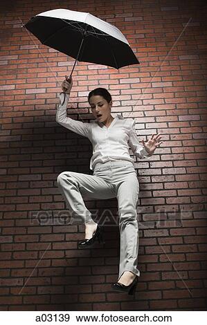 Studio shot of young woman falling holding umbrella View Large Photo Image Stock Photo - Studio shot of young woman falling holding umbrella. Fotosearch