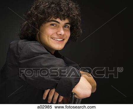 Stock Photography - Teenage boy (16-17) sitting backwards on chair, portrait. Fotosearch