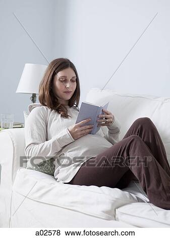Stock Photo - USA, California, San Francisco, pregnant woman lying and reading book on sofa. Fotosearch