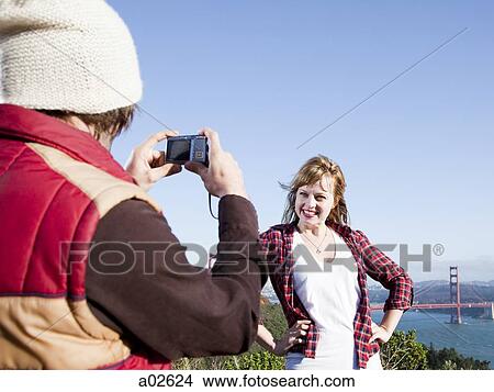 Picture - USA, California, San Francisco, young man taking picture of his girlfriend, Golden Gate Bridge in background. Fotosearch