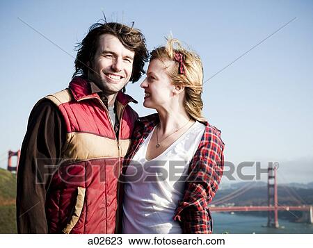 Stock Image - USA, California, San Francisco, young couple standing, Golden Gate Bridge in background. Fotosearch