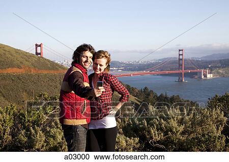 USA, California, San Francisco, young couple photographing themselves with Golden Gate Bridge in background, portrait View Large Photo Image Stock Image - USA, California, San Francisco, young couple photographing themselves with Golden Gate Bridge in background, portrait. Fotosearch