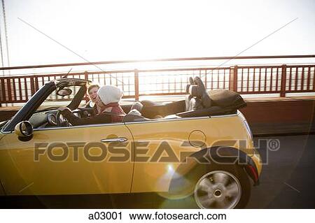 Stock Image - USA, California, San Francisco, young couple sitting car with Golden Gate Bridge in background, portrait. Fotosearch