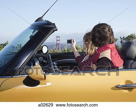 Stock Photo - USA, California, San Francisco, young couple sitting in car and taking picture of Golden Gate Bridge. Fotosearch