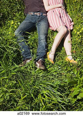 Stock Photo - USA, San Francisco, California, young couple lying on grass, low section. Fotosearch