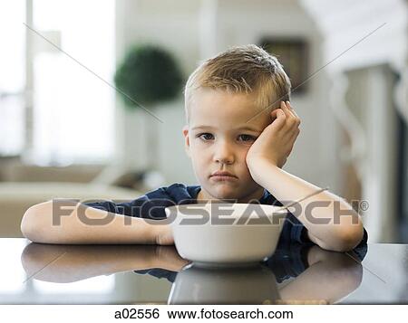 Stock Photograph - USA, Utah, Alpine, boy (6-7) resting cheek on hand by bowl. Fotosearch