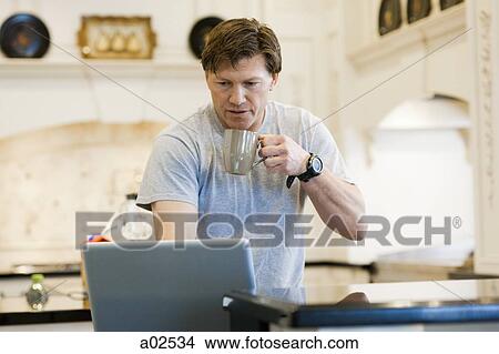 Picture - USA, Utah, Alpine, mature man looking at laptop and holding mug. Fotosearch