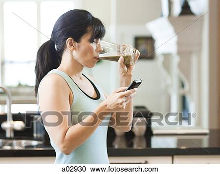 USA, Utah, Alpine, mid adult woman drinking juice and using mobile phone in kitchen View Large Photo Image Stock Image - USA, Utah, Alpine, mid adult woman drinking juice and using mobile phone in kitchen. Fotosearch