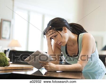 Stock Image - USA, Utah, Alpine, mid adult woman leaning to kitchen counter and holding letters in kitchen. Fotosearch