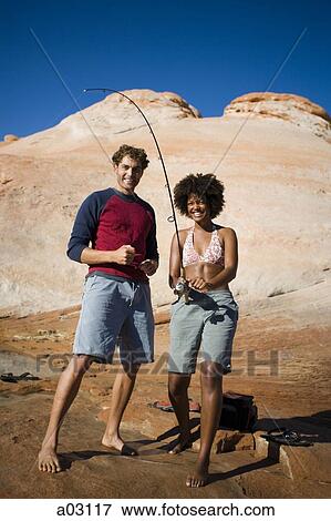 Stock Photo - USA, Utah, Lake Powell, young couple standing and fishing in the lake. Fotosearch
