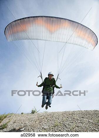 Stock Photo - USA, Utah, Lehi, mature man taking off with paraglide, low angle view. Fotosearch