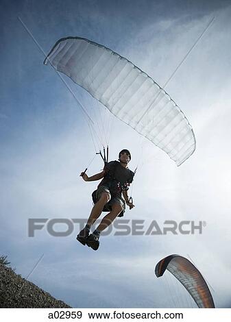 Stock Photo - USA, Utah, Lehi, mature man taking off with paraglide, low angle view. Fotosearch