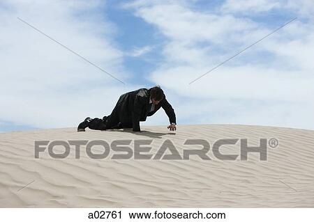Stock Image - USA, Utah, Little Sahara, mid adult businessman crawling over sand dune. Fotosearch