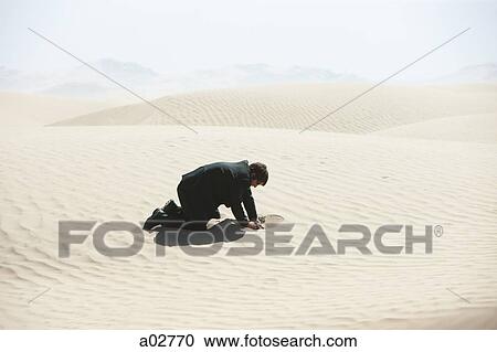Stock Image - USA, Utah, Little Sahara, mid adult businessman digging hole on desert. Fotosearch
