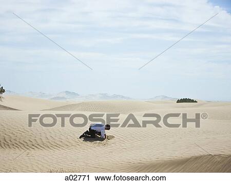 Stock Image - USA, Utah, Little Sahara, mid adult businessman digging hole on desert. Fotosearch