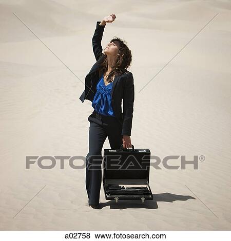 Stock Photo - USA, Utah, Little Sahara, young businesswoman standing on desert shielding sun with arm. Fotosearch