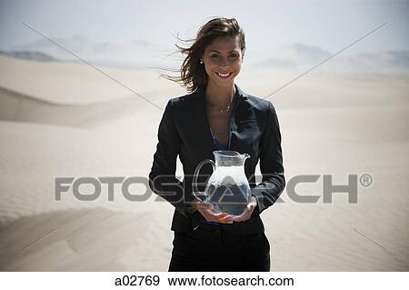 USA, Utah, Little Sahara, young businesswoman standing on desert holding jug of water View Large Photo Image Stock Photo - USA, Utah, Little Sahara, young businesswoman standing on desert holding jug of water. Fotosearch